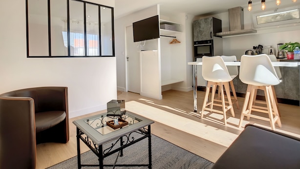 Une cuisine moderne avec des meubles blancs, un four encastré et un coin repas comprenant des chaises blanches et une table en verre.
