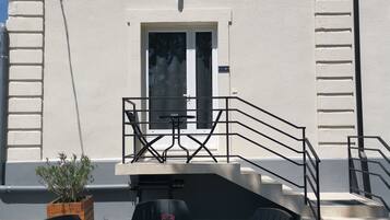 Un espace extérieur aménagé avec une table ronde et quatre chaises, un pot de fleurs et un escalier menant à un niveau supérieur.