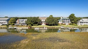 A waterfront property with multiple buildings, a dock with boats, and a grassy area with reeds.