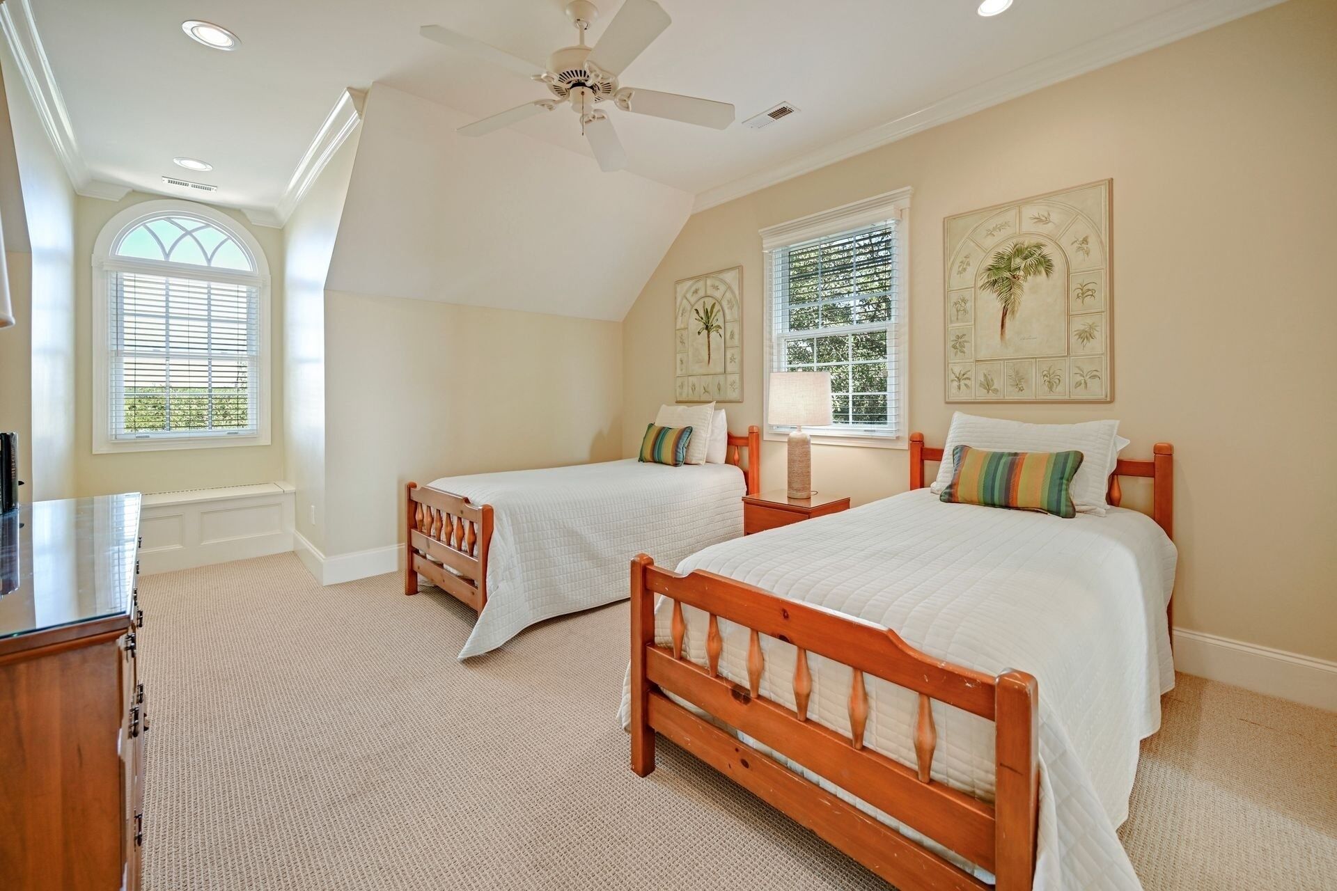A bedroom with two wooden beds, a ceiling fan, and large windows with blinds.