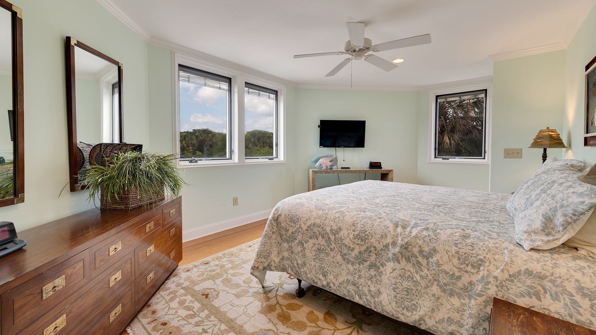 A bedroom with a bed, dresser, TV, and windows.
