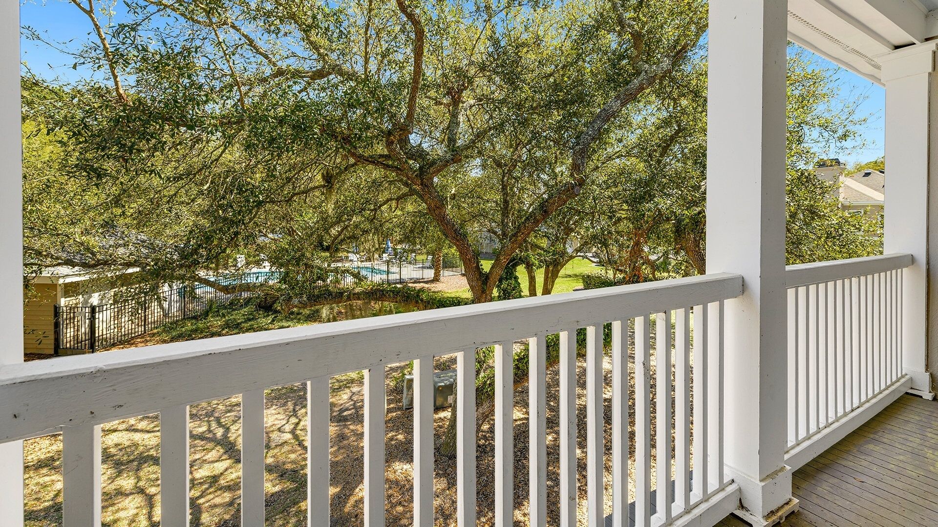 A covered porch with a white railing, overlooking a backyard with trees and a fenced area.