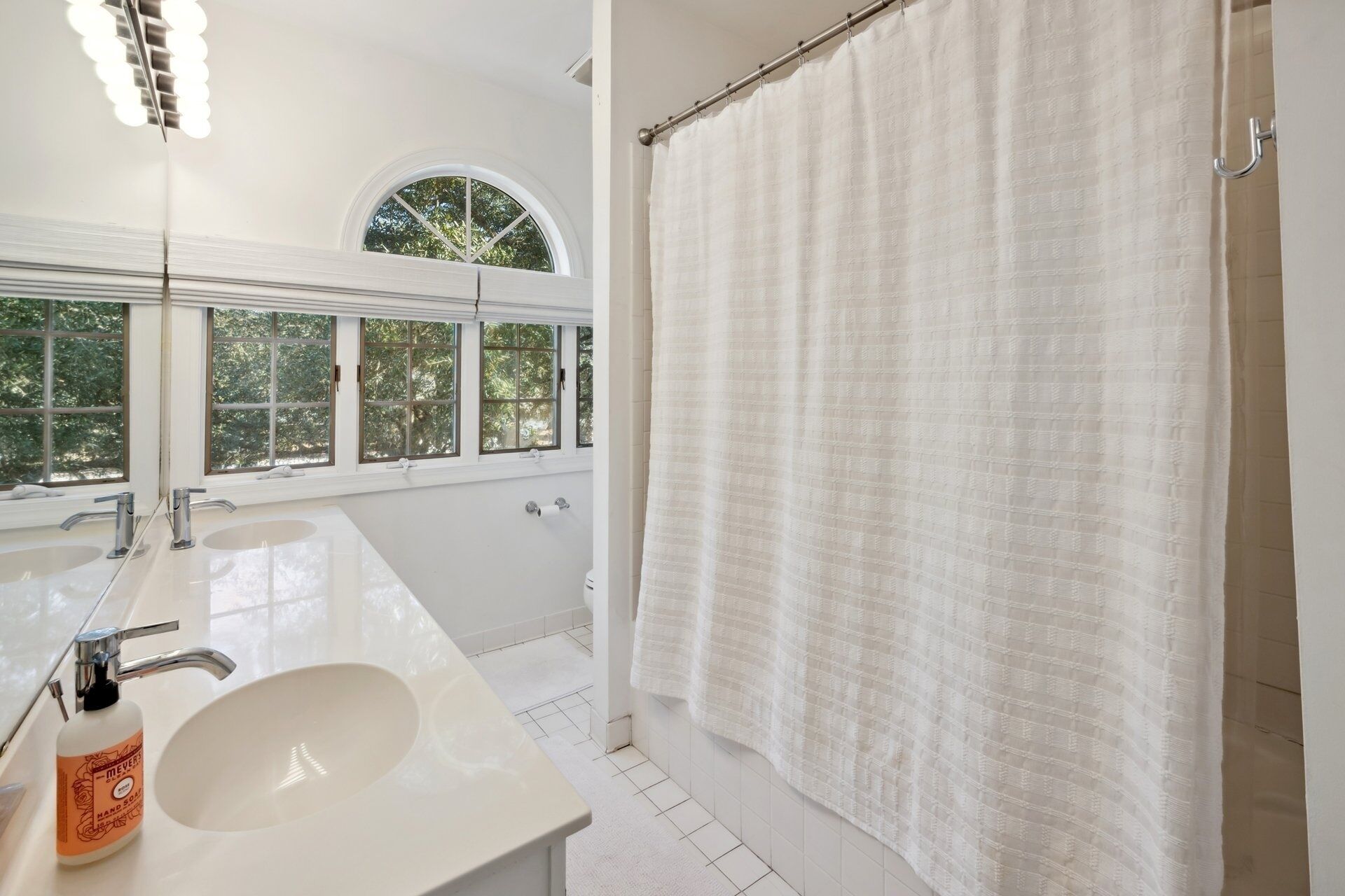 A bathroom with two sinks, a shower curtain, and a window with a view of trees.