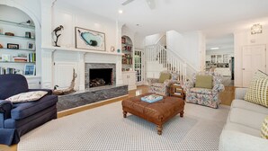 A spacious living room with a fireplace, a staircase, and a bookshelf. - Relax And Be Tranquil By The Sea 5 Bedroom Home by Peace Vacations (Georgetown)