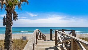 A wooden boardwalk leading to a beach with a palm tree and ocean view.