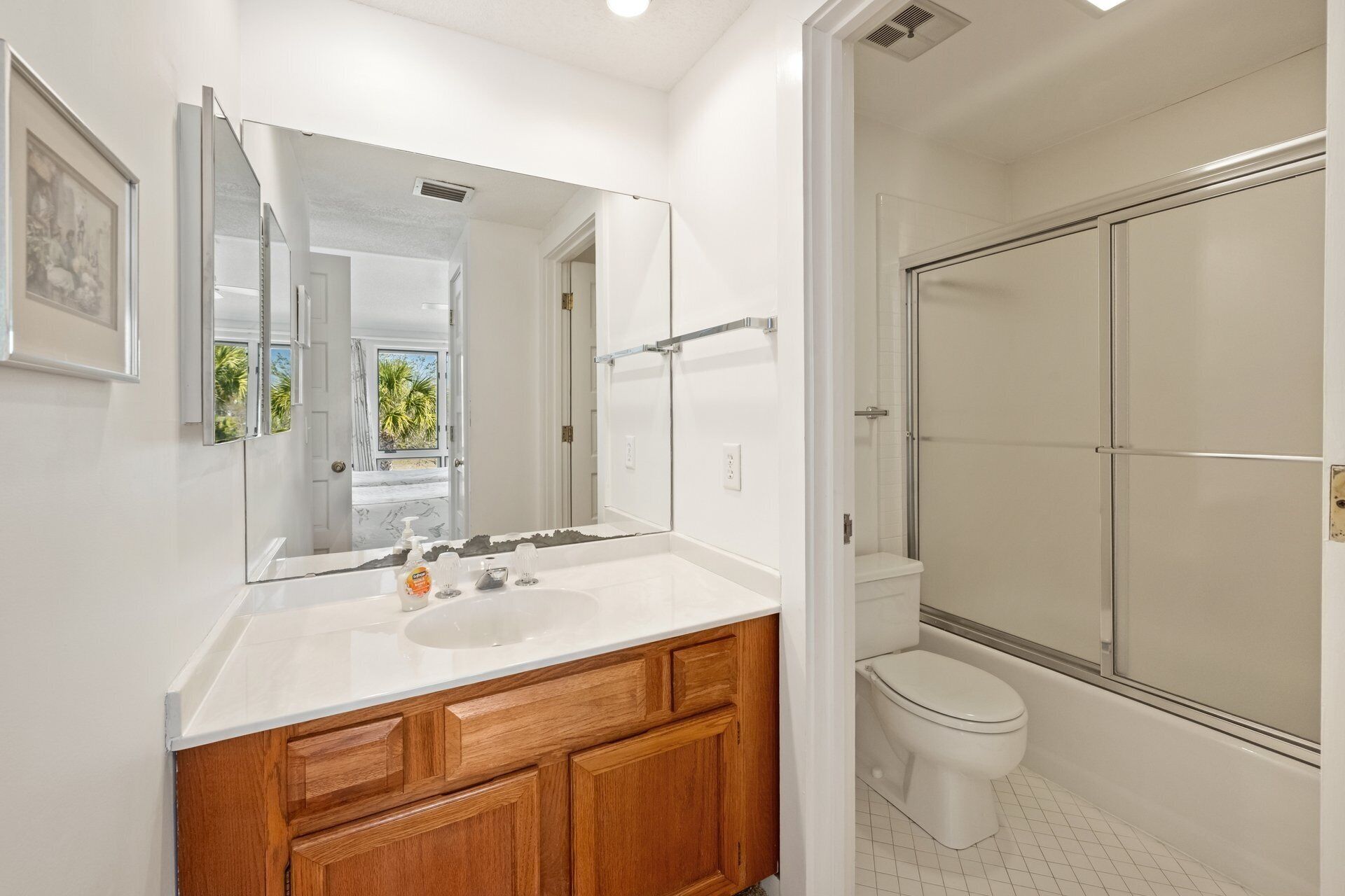 A modern bathroom with a large mirror, wooden vanity, white sink, and a glass-enclosed shower.