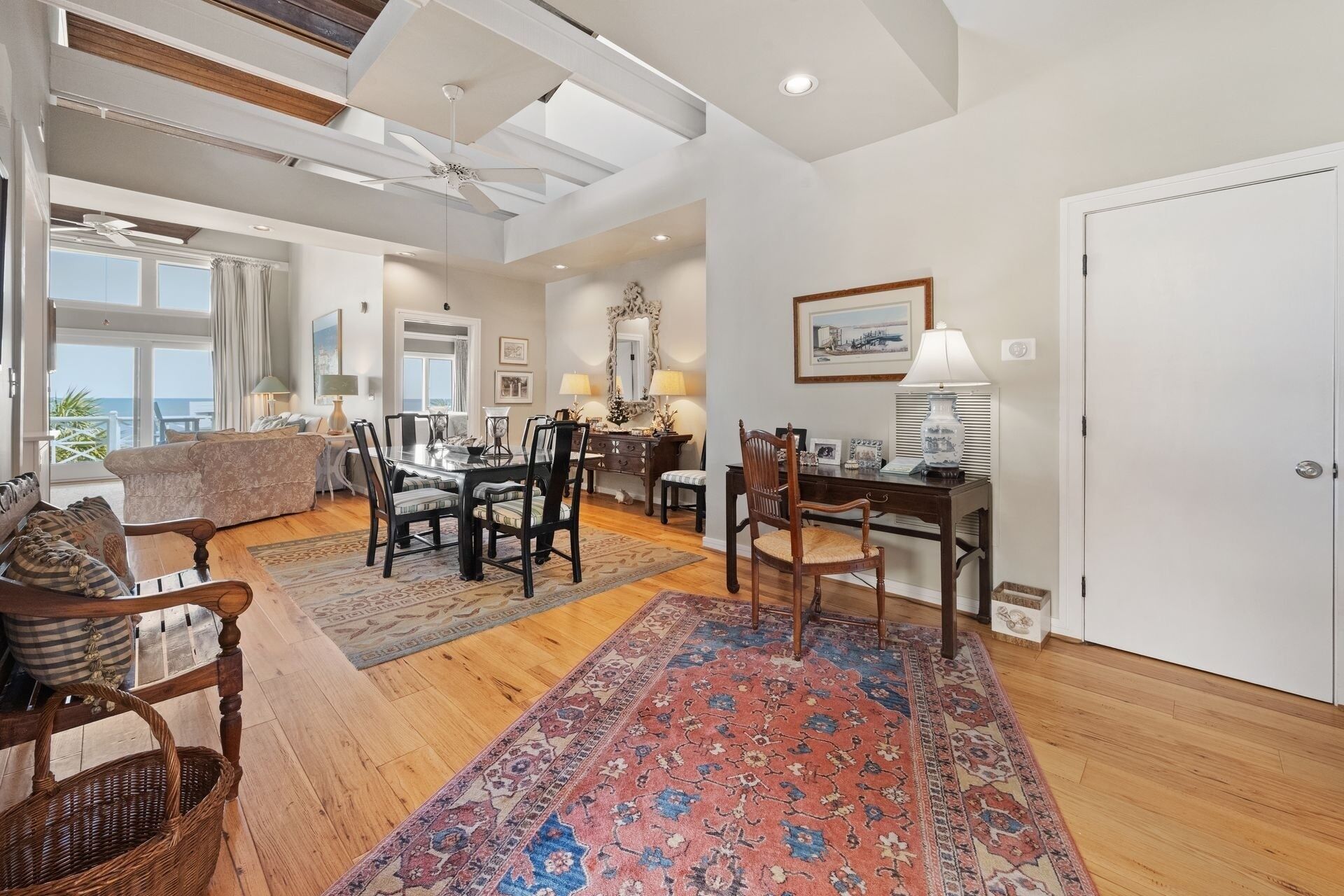 A spacious living area with a dining table, chairs, and a large rug. There is a view of the ocean through a large window.