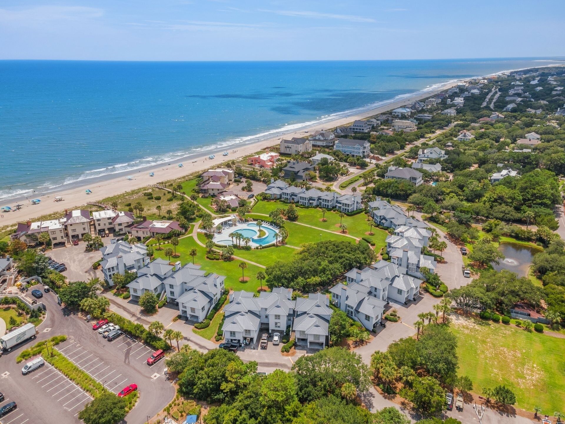 An aerial view of a coastal residential area with a swimming pool, houses, and a beach.