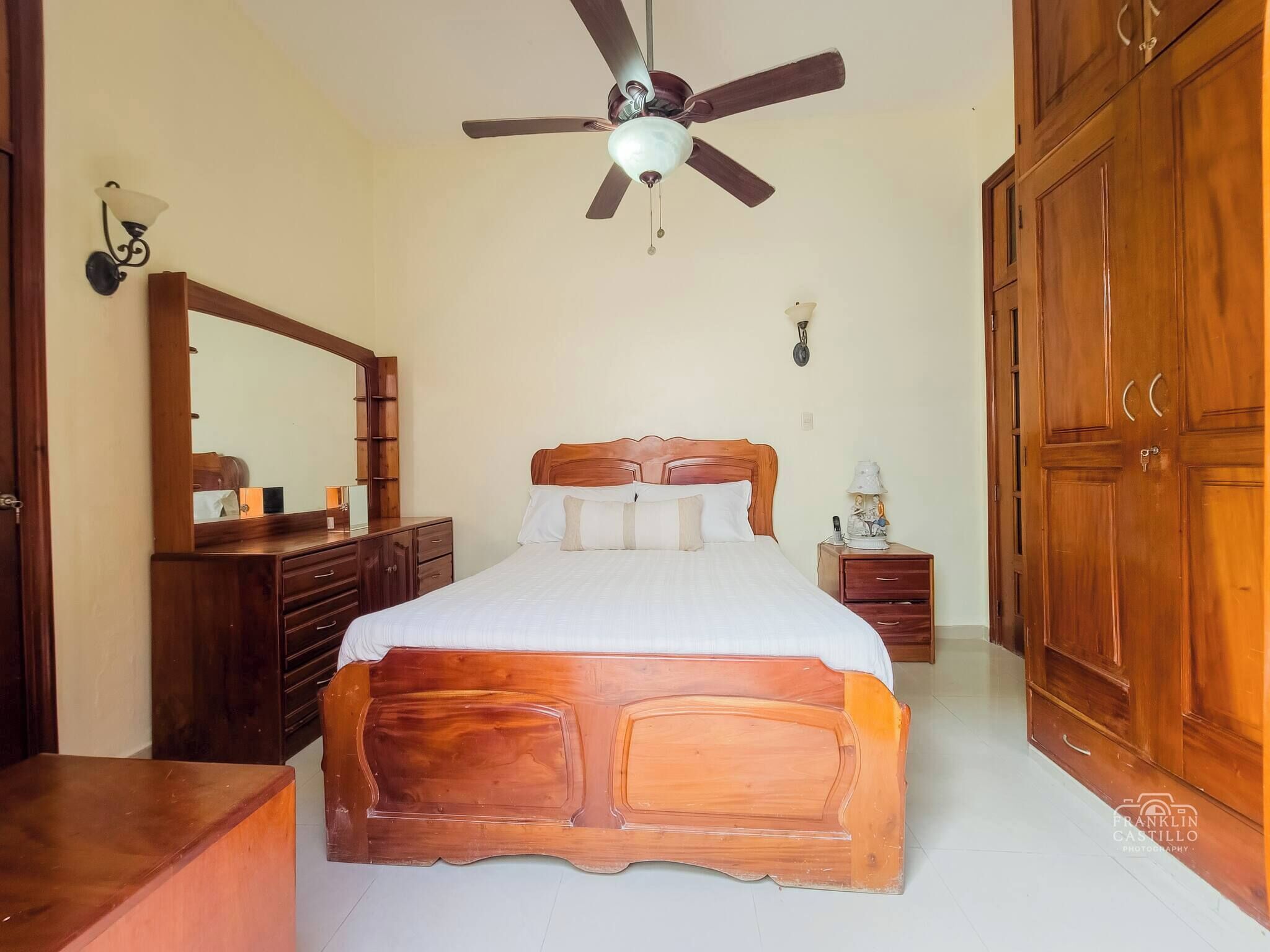 A bedroom with a wooden bed, a ceiling fan, a dresser, a nightstand, and a wardrobe.