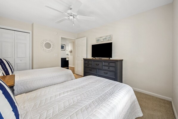 A bedroom with two beds, a dresser, a ceiling fan, and a television. - Relax At Pawleys After Dark 2 Bedroom Condo by Peace Vacations (Pawleys Island)