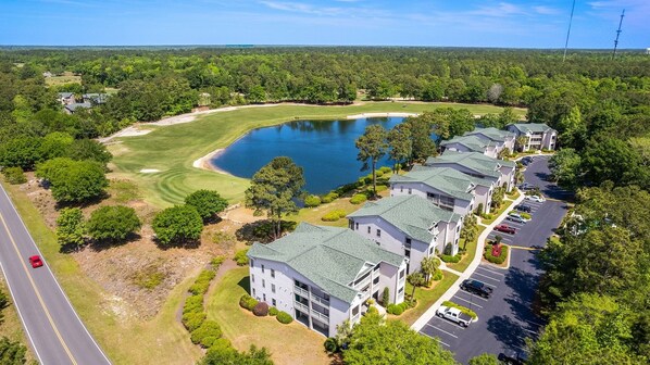 Ein Golfplatz mit einem See, umgeben von Wohngebäuden mit Balkonen und Parkplätzen.
