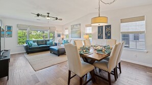 A spacious living room with a dining area, large windows, and a ceiling fan.