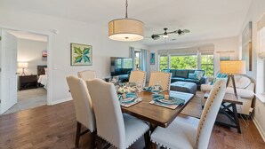 A dining area with a wooden table set for six, surrounded by upholstered chairs with a light fabric.