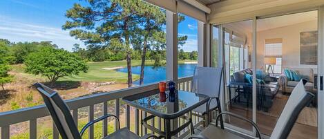 A balcony with a table and chairs overlooking a golf course and a lake.