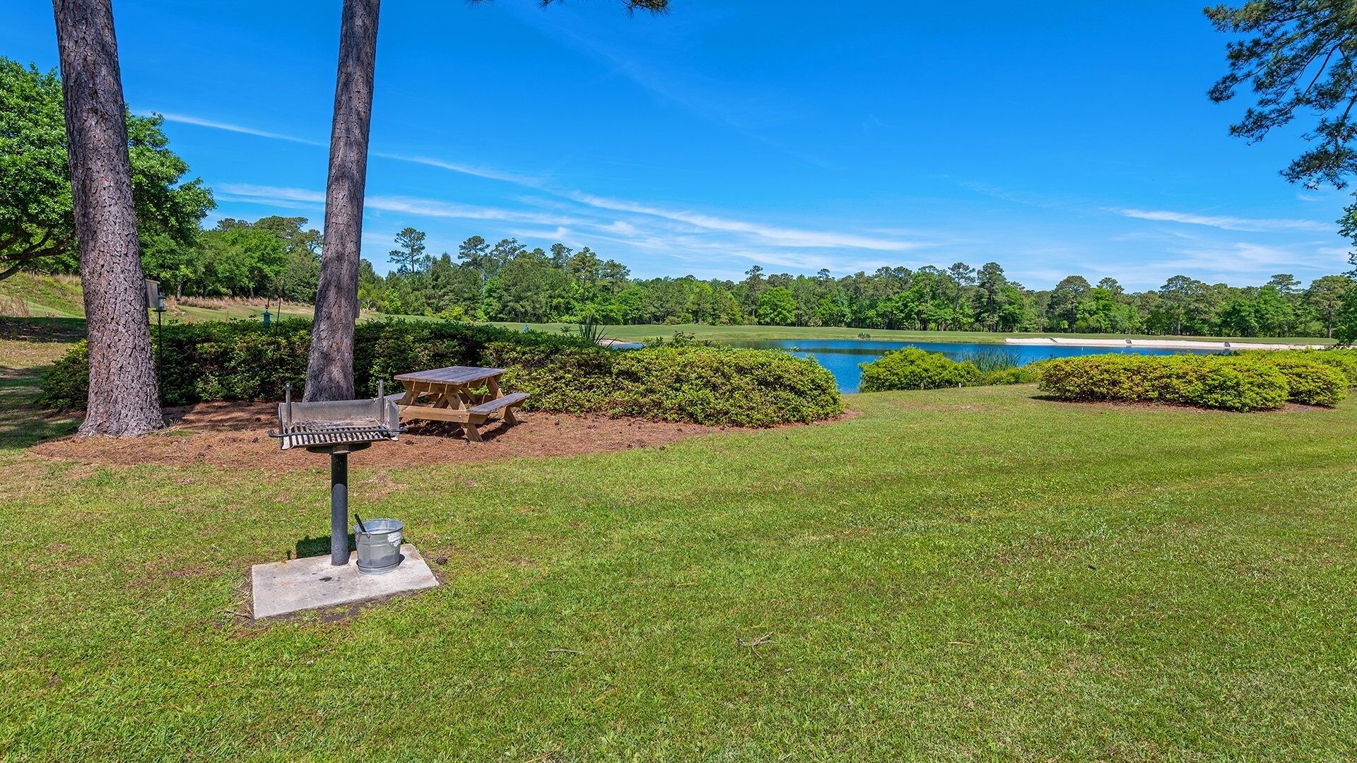 A well-maintained grassy area with a bird feeder, picnic tables, and a lake in the background.