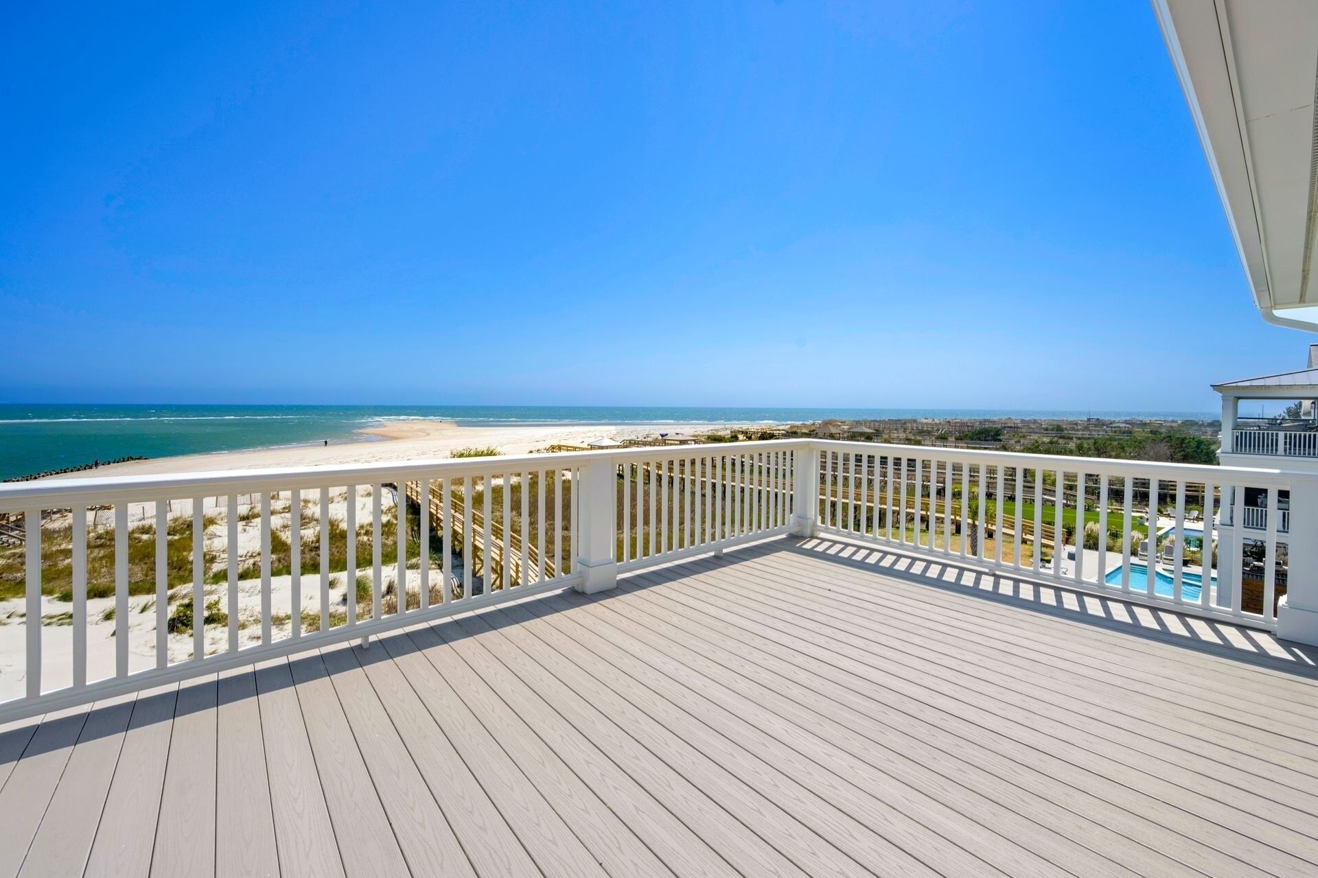 Ein Holzdeck mit weißer Reling mit Blick auf einen Strand und den Ozean.