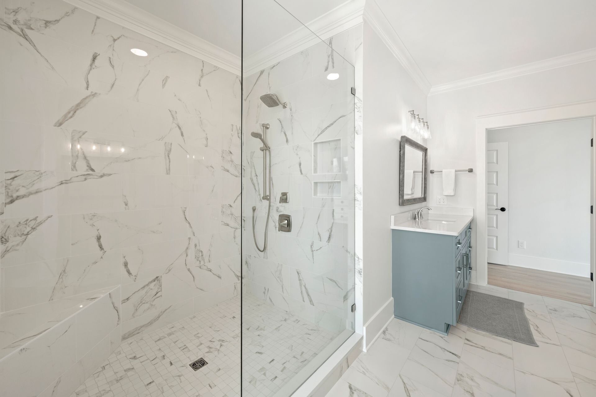 Une salle de bain moderne avec une douche à parois de verre, des carreaux de marbre, un meuble-lavabo bleu et un miroir.