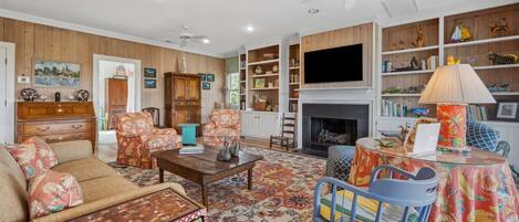A cozy living room with a fireplace, wooden paneling, and a bookshelf filled with books and decorative items.
