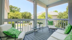 Relax on the covered porch with a view of the surrounding neighborhood, featuring a glass-top table and two cushioned chairs.