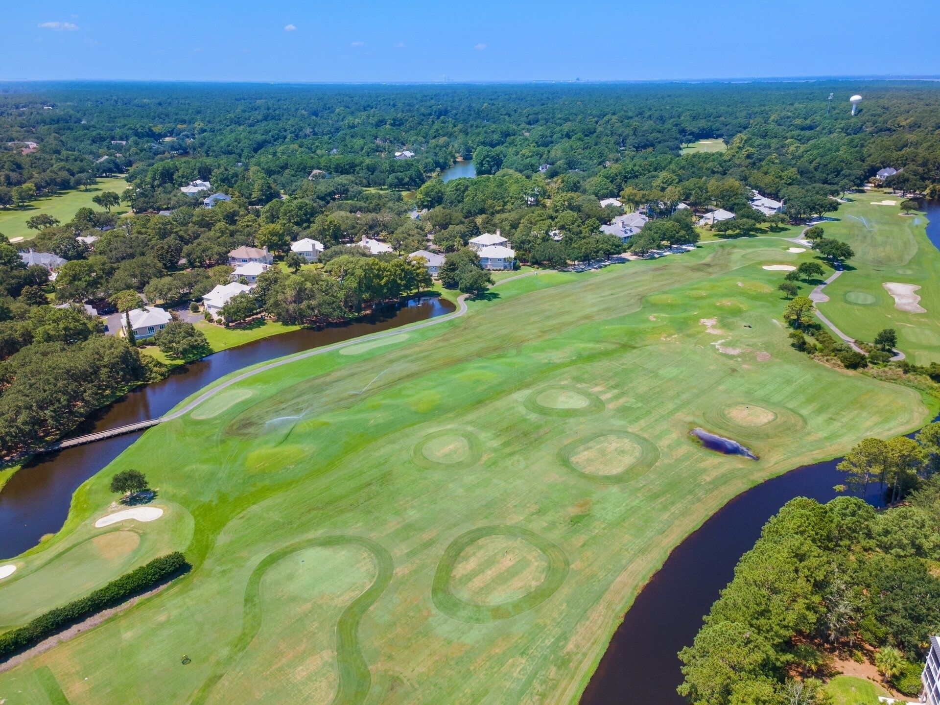 An aerial view of a golf course with a river running through it, surrounded by residential areas.