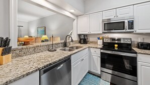 A modern kitchen with white cabinets, granite countertops, stainless steel appliances including a microwave, stove, and dishwasher, and a sink.