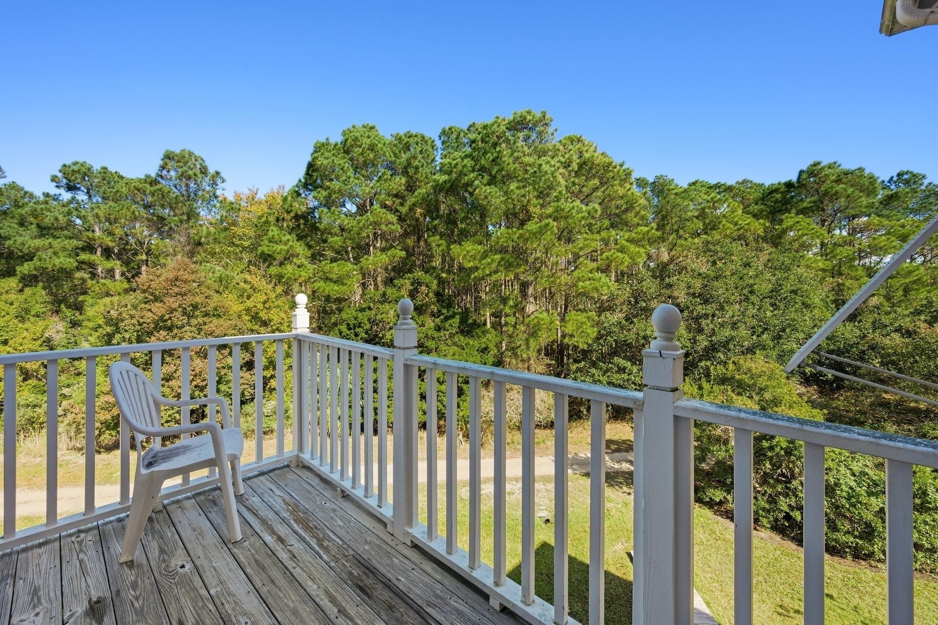 A wooden deck with white railings and a white plastic chair.