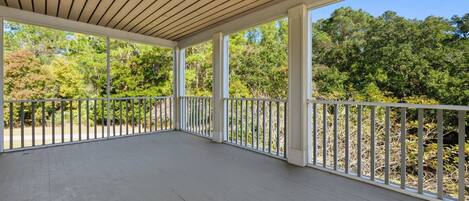 A covered porch with a wooden ceiling and white railings, surrounded by trees.