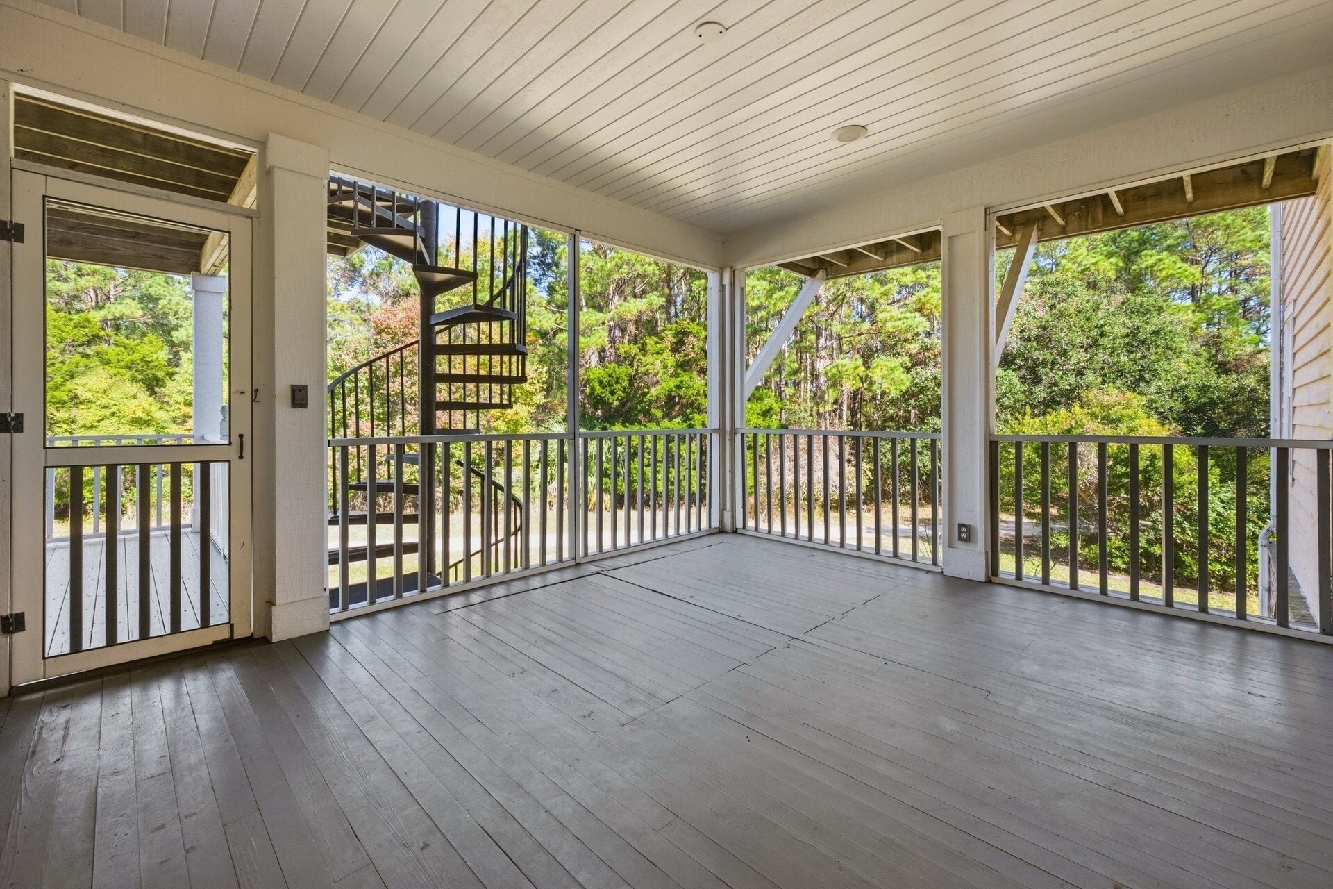 A spacious covered porch with a spiral staircase leading to a deck.