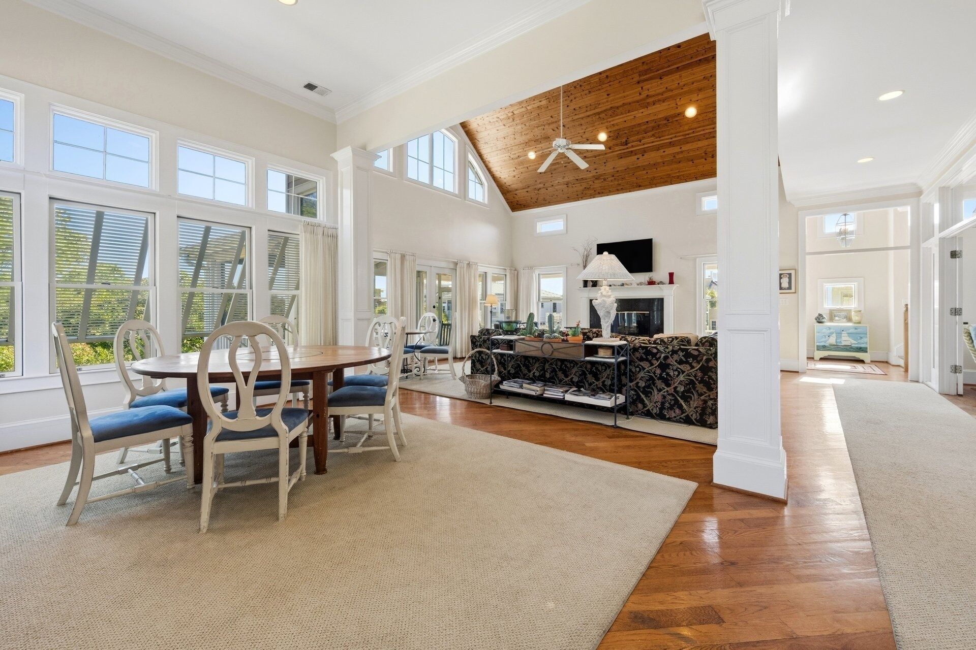 A spacious living area with a high ceiling, large windows, and a fireplace.