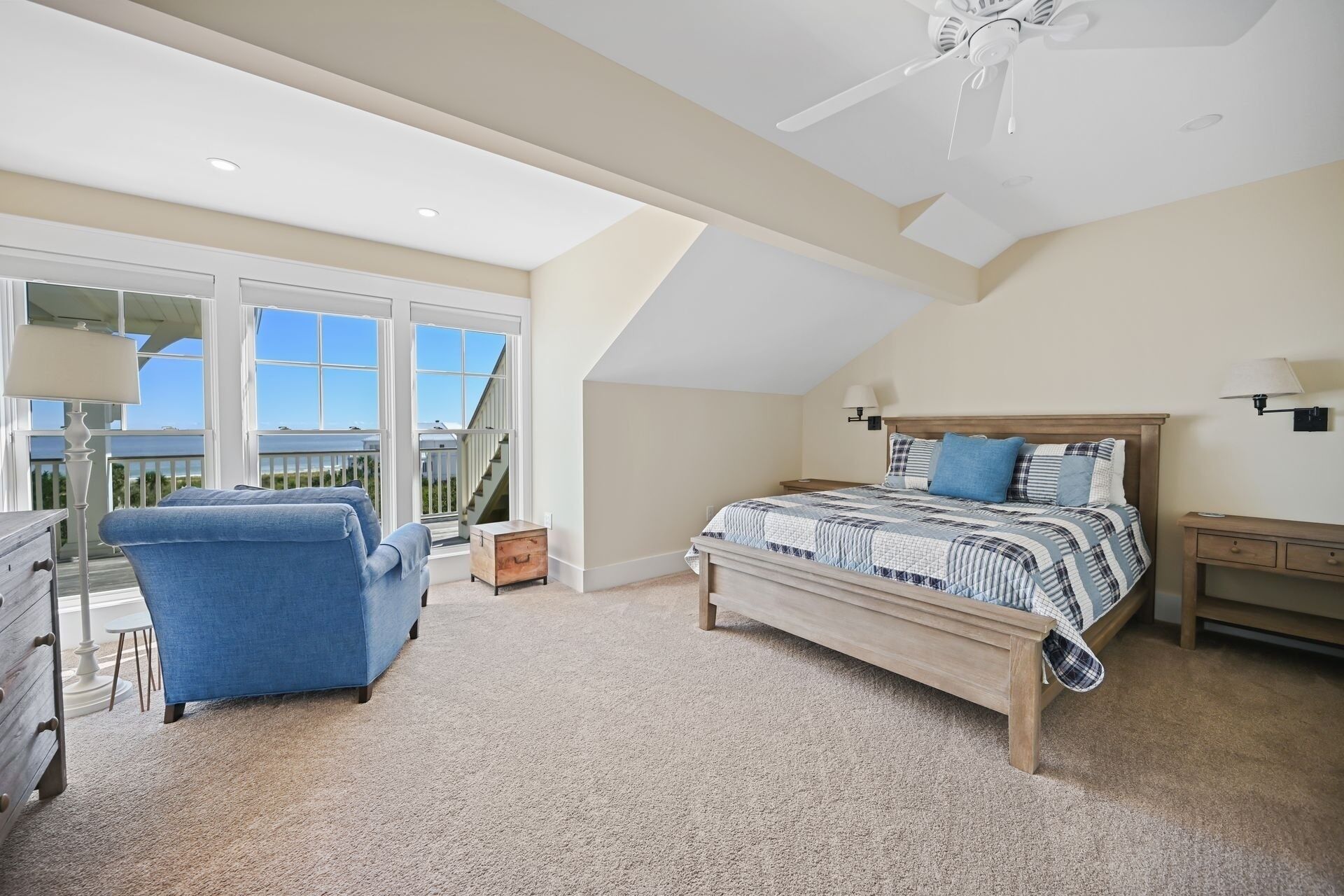 A bedroom with a large bed, a chair, a desk, and a balcony with glass doors.