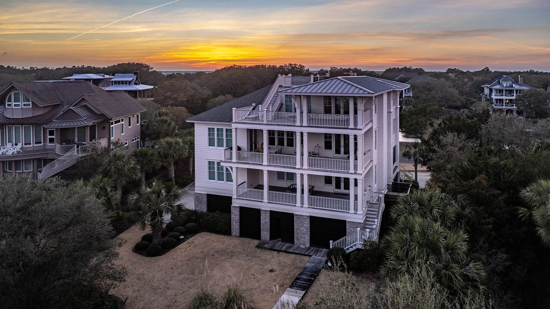 Ein mehrgeschossiges Haus mit Balkon, umgeben von Bäumen und einem Sonnenuntergang im Hintergrund.