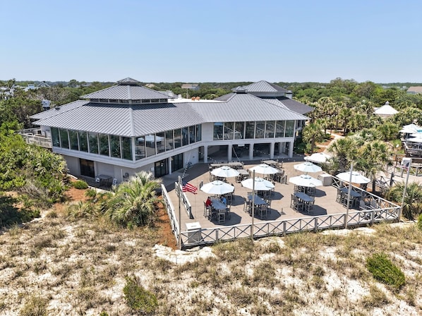 A modern building with a glass facade, outdoor seating area with umbrellas, and a surrounding natural landscape.
