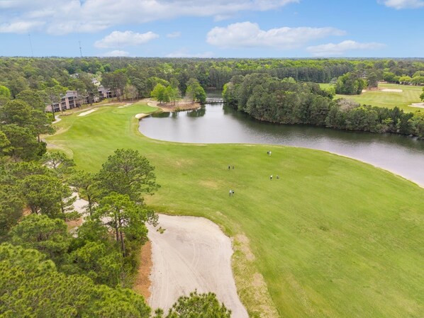 A golf course with a lake, surrounded by trees and a building complex. - Located On The Ground Level And Across From The Pool With Pass To Huntington State Park! 2 Bedroom Condo by Peace Vacations (Pawleys Island)