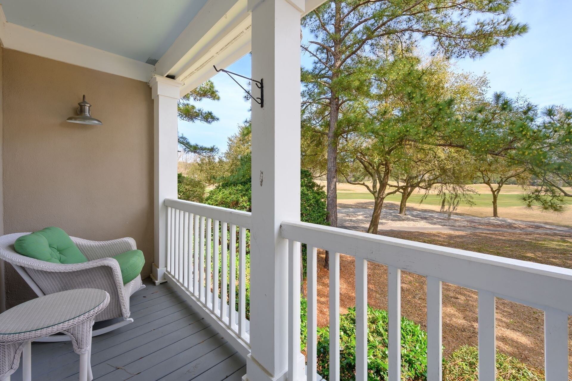 A porch with white railings, a wicker chair with a green cushion, and a view of trees and a golf course.
