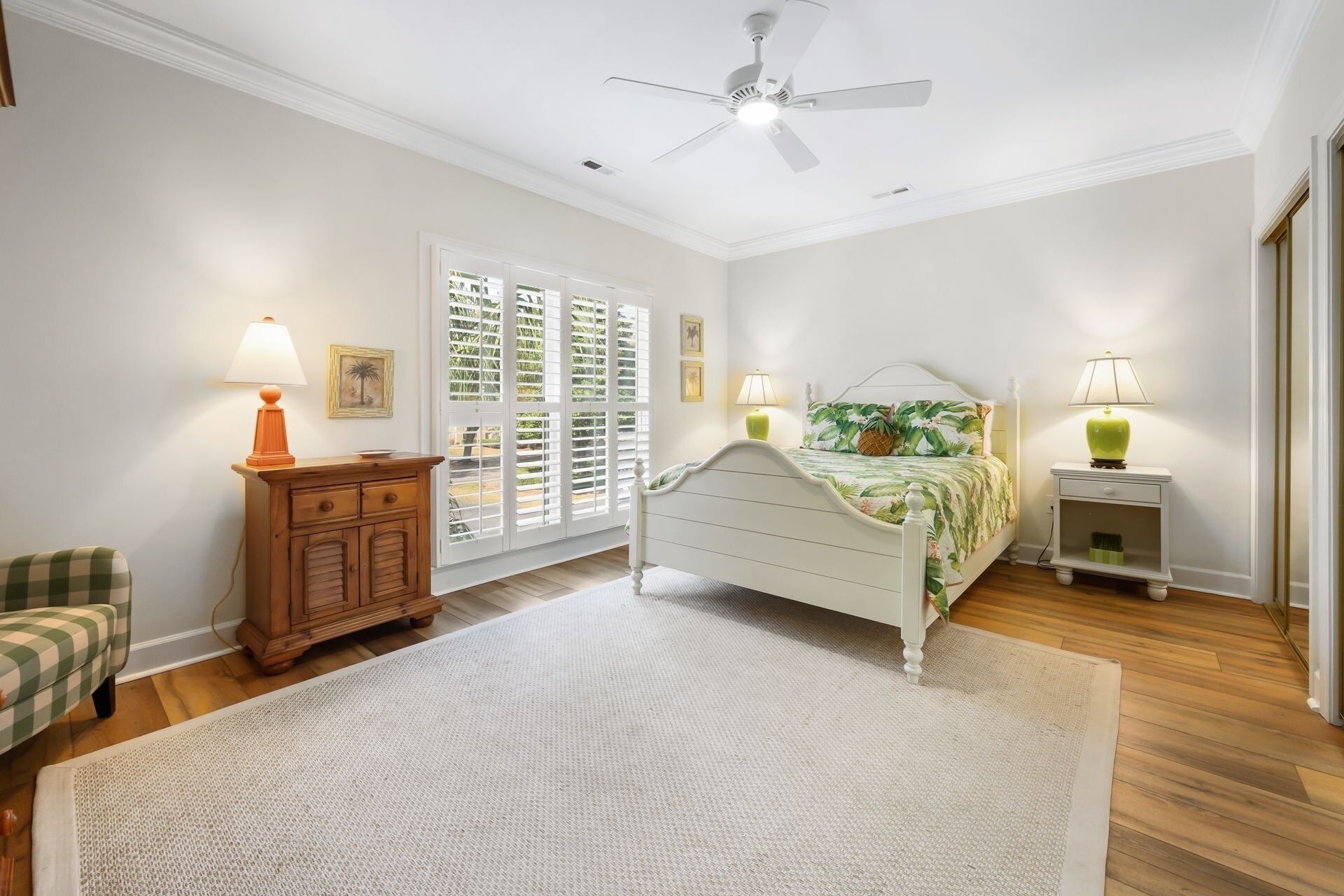 A bedroom with a bed, nightstands, a dresser, a ceiling fan, and a window with shutters.