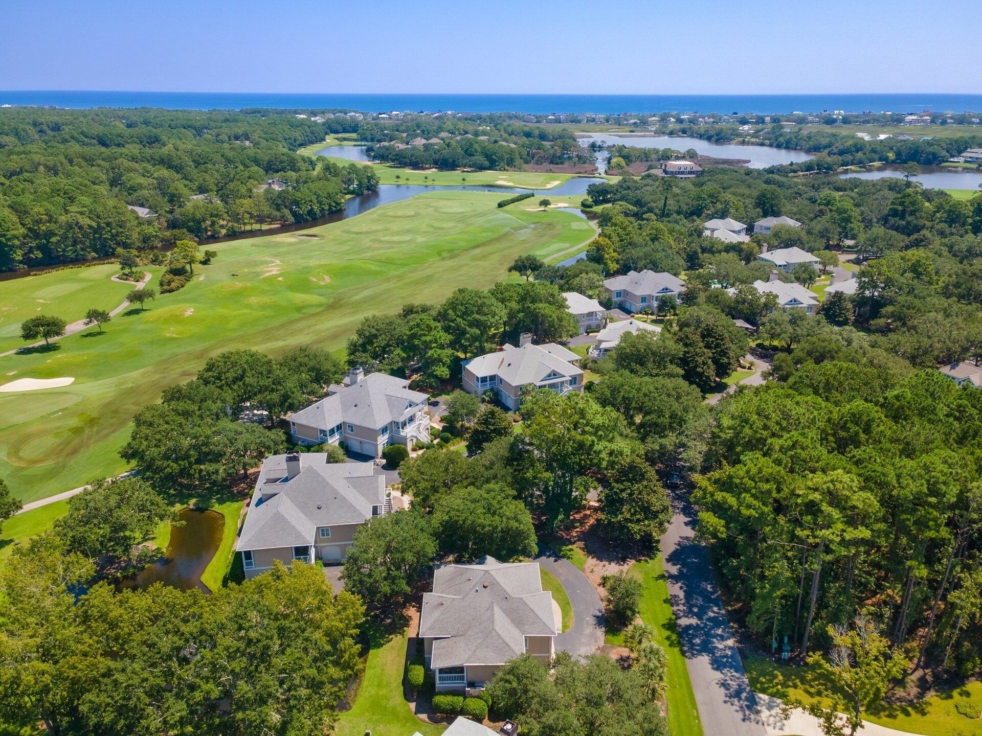 An aerial view of a residential area with houses, a golf course, and a body of water.