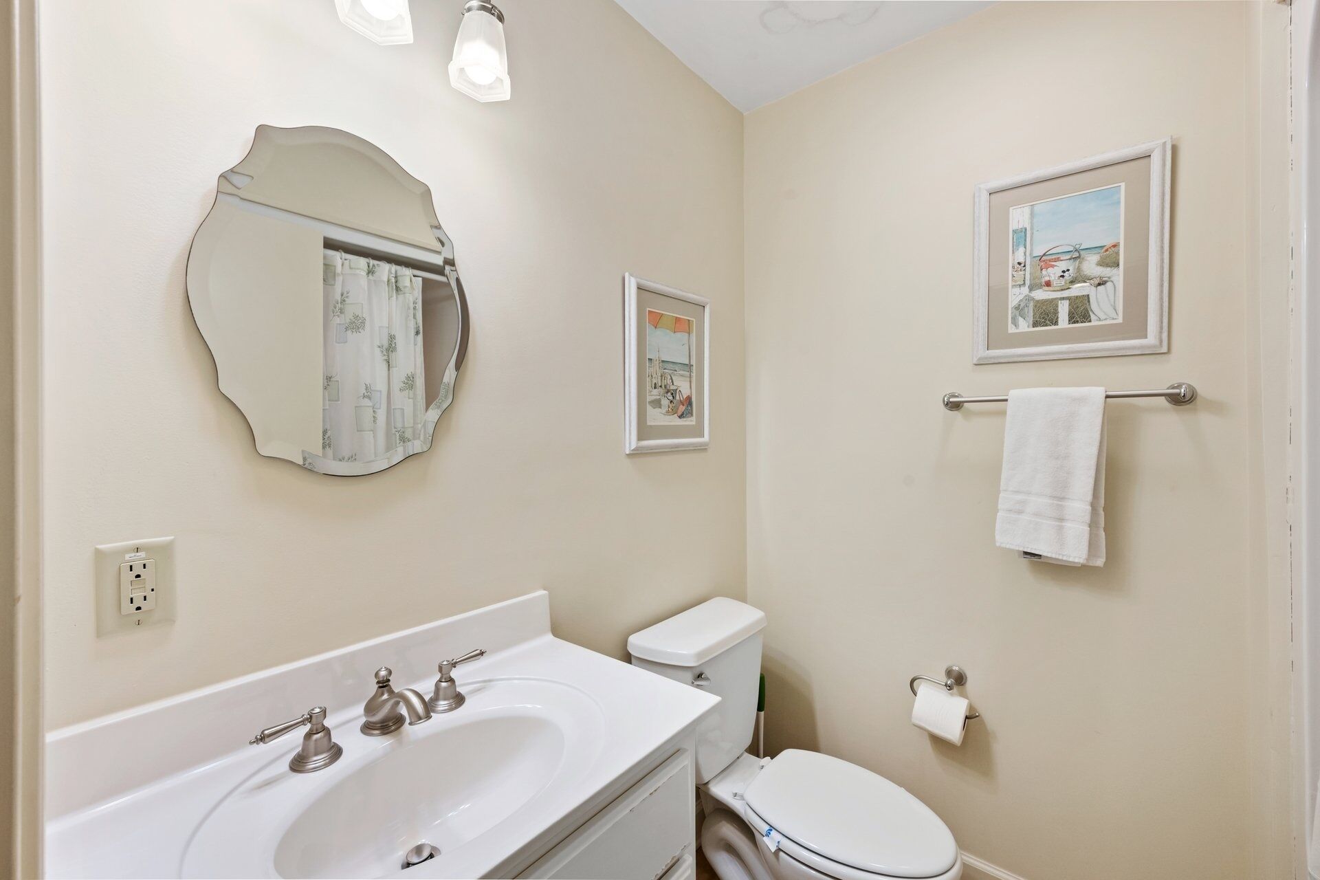 Ein Badezimmer mit einem weißen Waschbecken, einer Toilette, einem Spiegel und zwei gerahmten Bildern an der Wand.