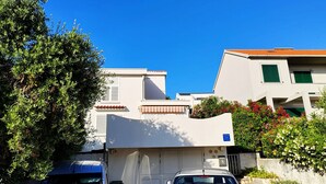 Un immeuble résidentiel à la façade blanche, aux volets verts et au toit recouvert de tuiles rouges.