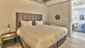 Un dormitorio moderno con una cama grande, mesitas de noche y una puerta visible que da a otra habitación.