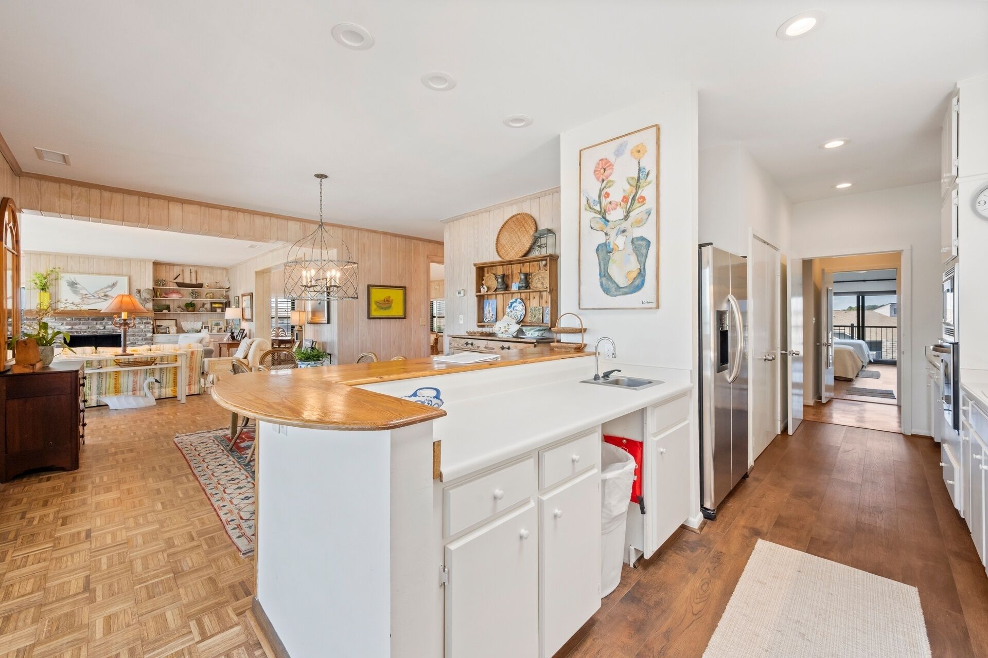 A spacious kitchen with a central island, white cabinetry, and a large painting above the sink.
