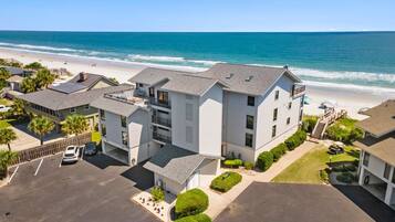 A beachfront property with multiple buildings, a parking lot, and a view of the ocean.