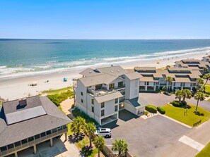 A beachfront property with multiple buildings, a parking area, and a view of the ocean.