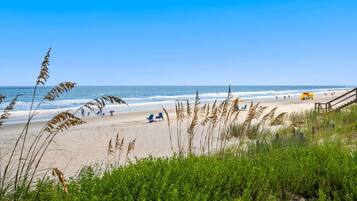 A beach with clear skies, a sandy shore, and a wooden staircase leading down to the water.