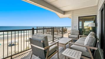 A balcony with a view of the beach, furnished with wicker chairs and a table.
