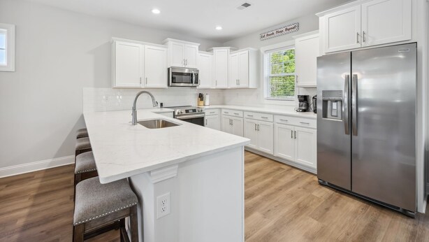 A modern kitchen with white cabinetry, a stainless steel refrigerator, a built-in microwave, and a bar stool.