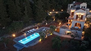 A pool with lounge chairs, a stone structure with a balcony, and a forested area.