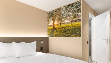 A hotel room with a large bed, a headboard, a wall-mounted light, and a door.