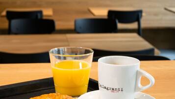 Ein Frühstücksbrett mit einem Croissant, einem Glas Orangensaft und einer weißen Tasse mit Logo auf einem Tisch in einem Essbereich mit Blick auf einen Sonnenuntergang.