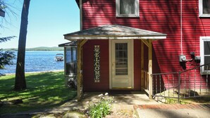 A red house with a 'WELCOME' sign, a dock, and a lake view. - Traditional Waterfront Maine Cottage on Long Lake with great swimming. (Naples)