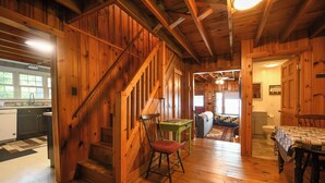 A wooden interior with a staircase, a dining table, and a kitchen area. - Traditional Waterfront Maine Cottage on Long Lake with great swimming. (Naples)